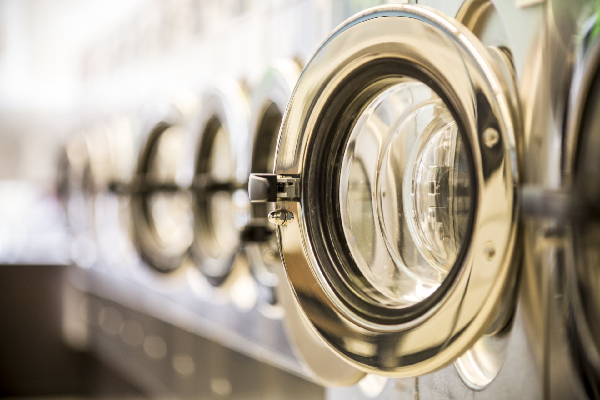 A close view down a row of commercial washing machines with open, gold-trimmed round doors.