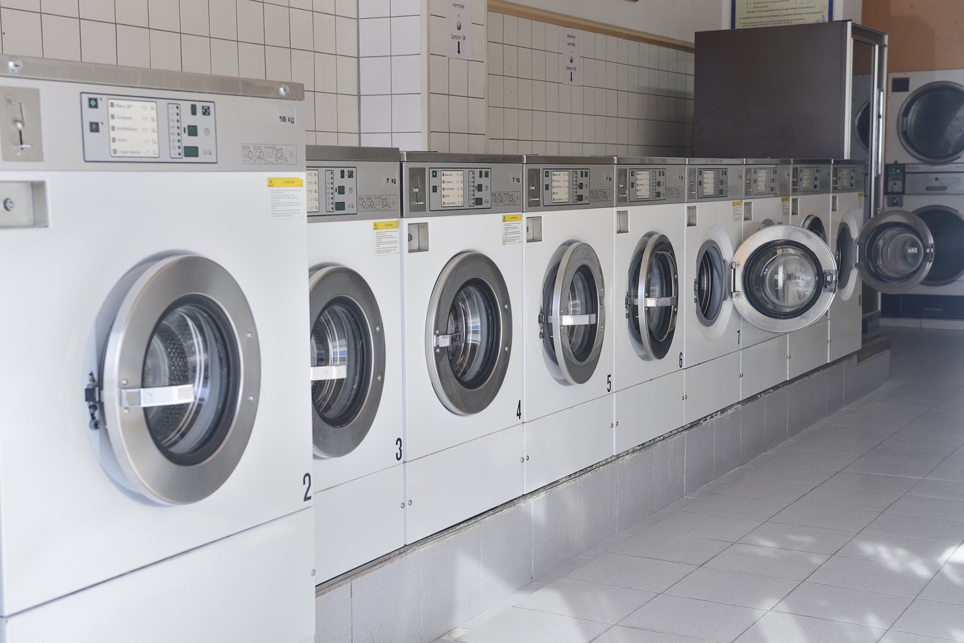 A row of coin-operated washing machines with their doors open in a laundromat