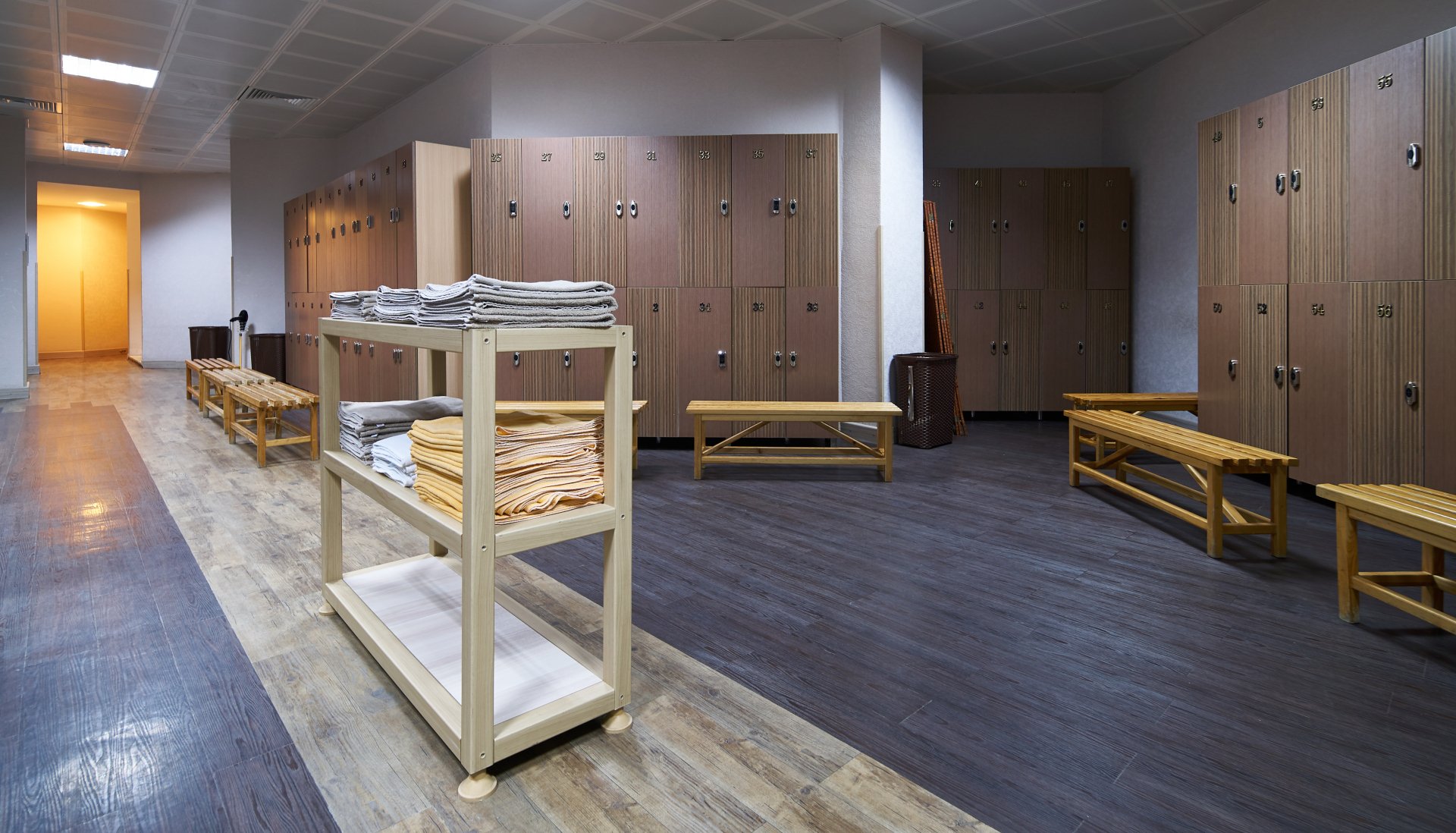 A health club locker room with a cart of folded towels beside rows of lockers and benches.