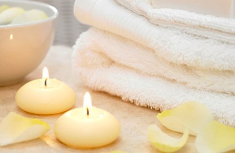 Lit floating candles beside folded white spa towels and rose petals.
