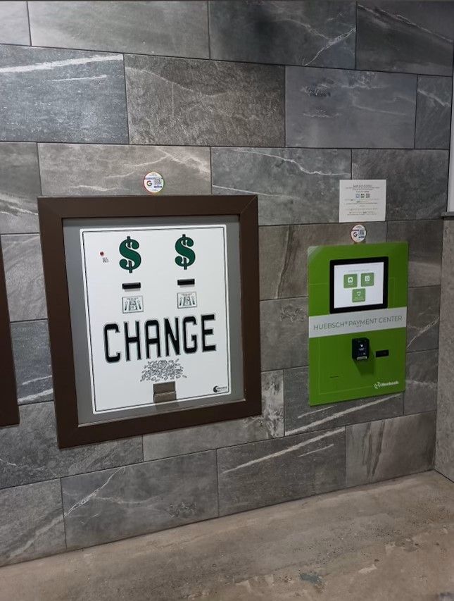 A coin-and-bill 'Change' machine mounted on a stone-tile wall next to a green Huebsch payment kiosk.