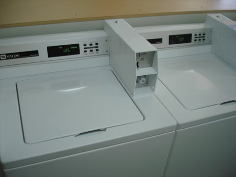 Two coin-operated top-load washing machines with a coin box mounted between them.