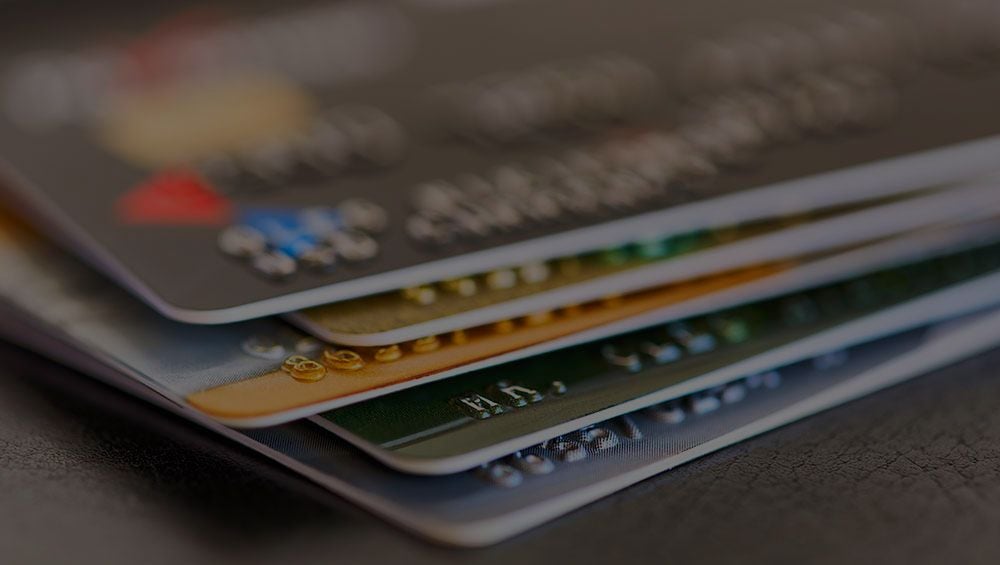 A fanned stack of credit and debit cards, close up, on a dark surface.
