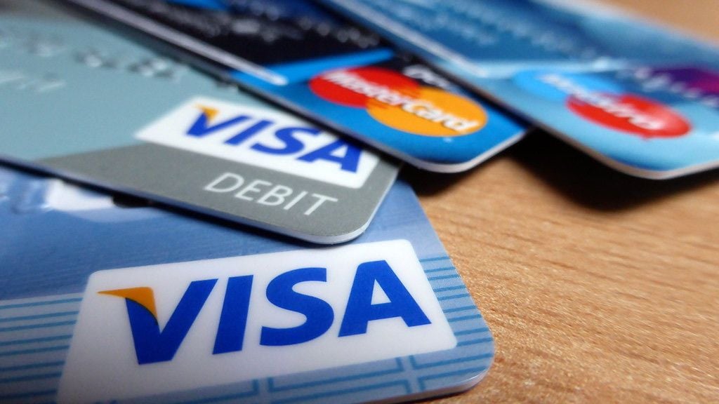 A spread of Visa and Mastercard credit and debit cards on a wooden table.