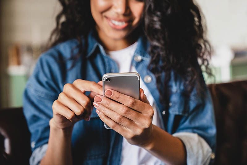 A smiling customer in a denim jacket paying for a laundry cycle on her phone.