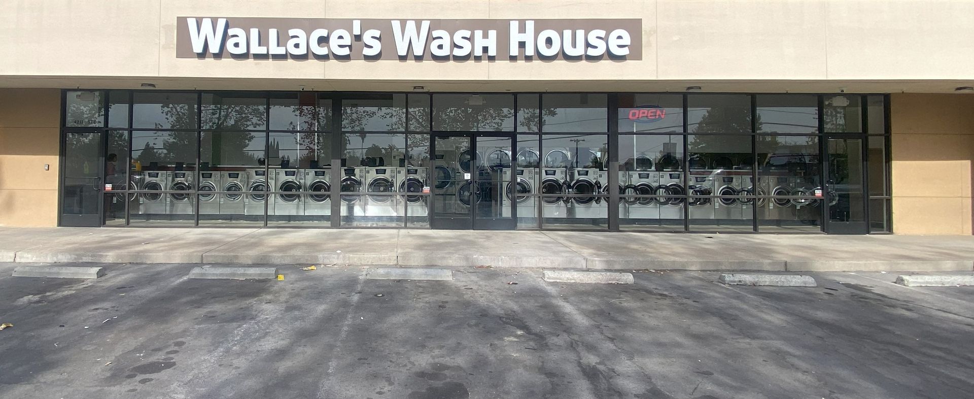 The Wallace's Wash House storefront, with large channel-letter signage above a glass front lined with washers and an illuminated 'Open' sign.
